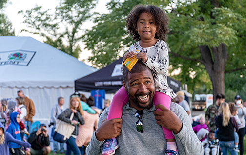 Man laughing while holding smiling child on shoulders