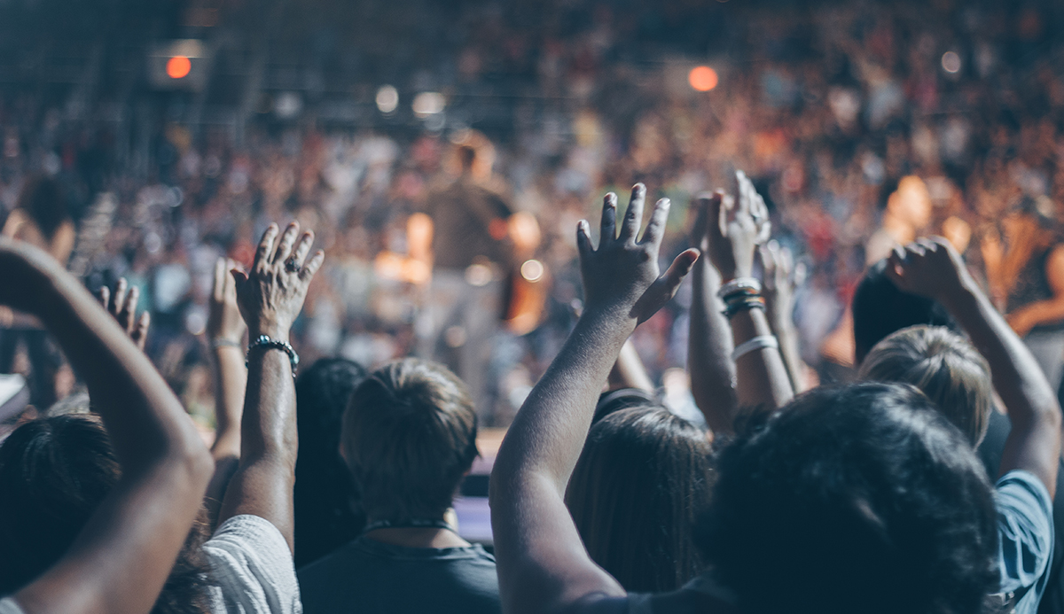 Large crowd at concert with hands in the air